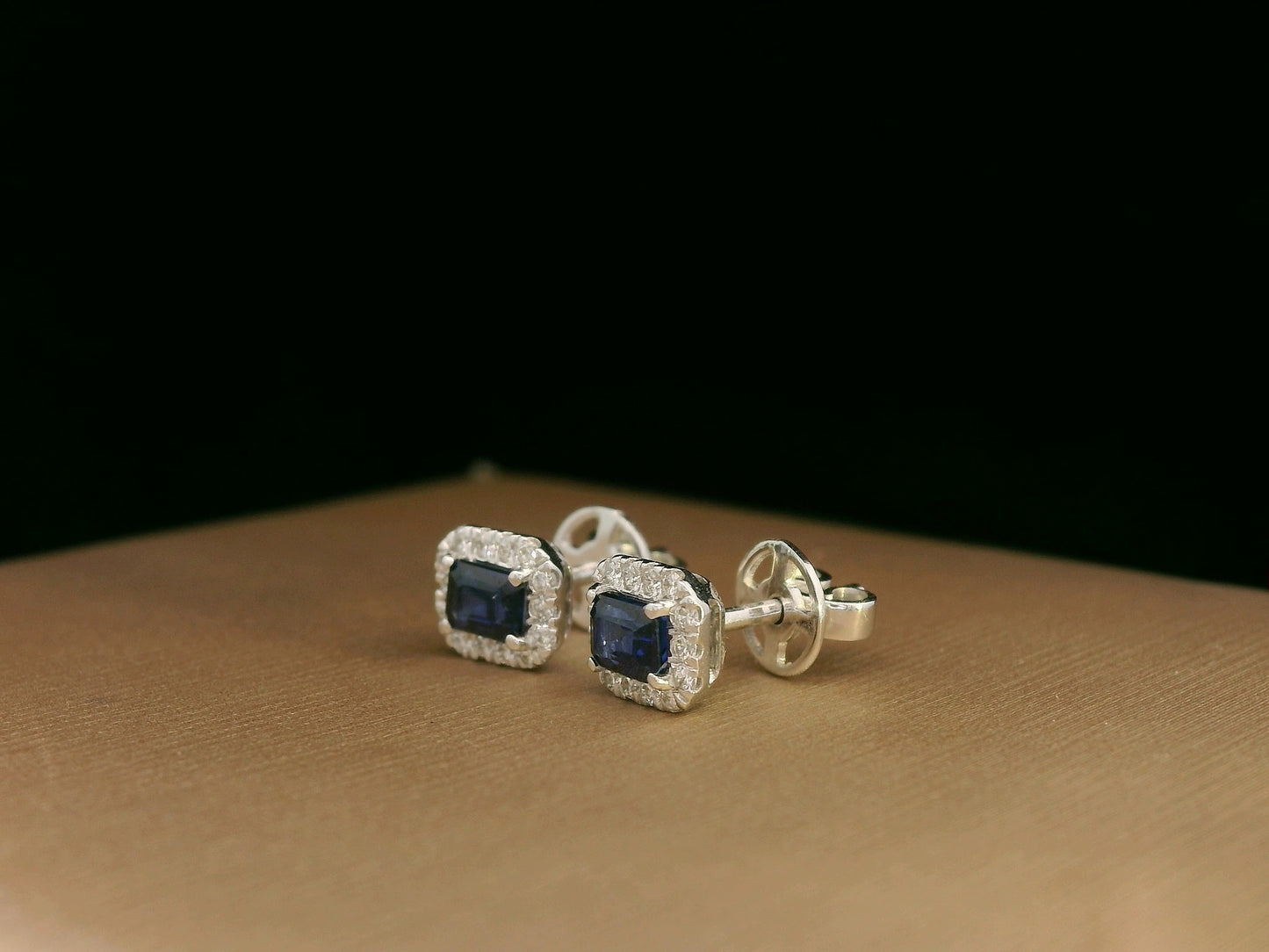 Minimalist 18K white gold halo stud earrings with emerald-cut blue sapphires and diamond accents 