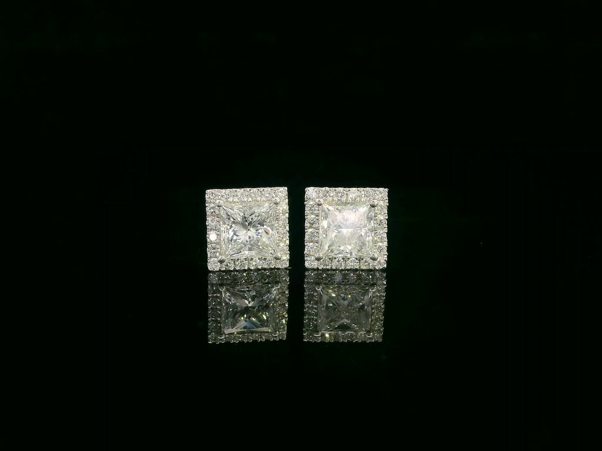 Princess cut diamond halo stud earrings in 18K white gold featuring GIA certified 1.01 carat E color VS2 diamonds with halo accents by Emirates Diamonds