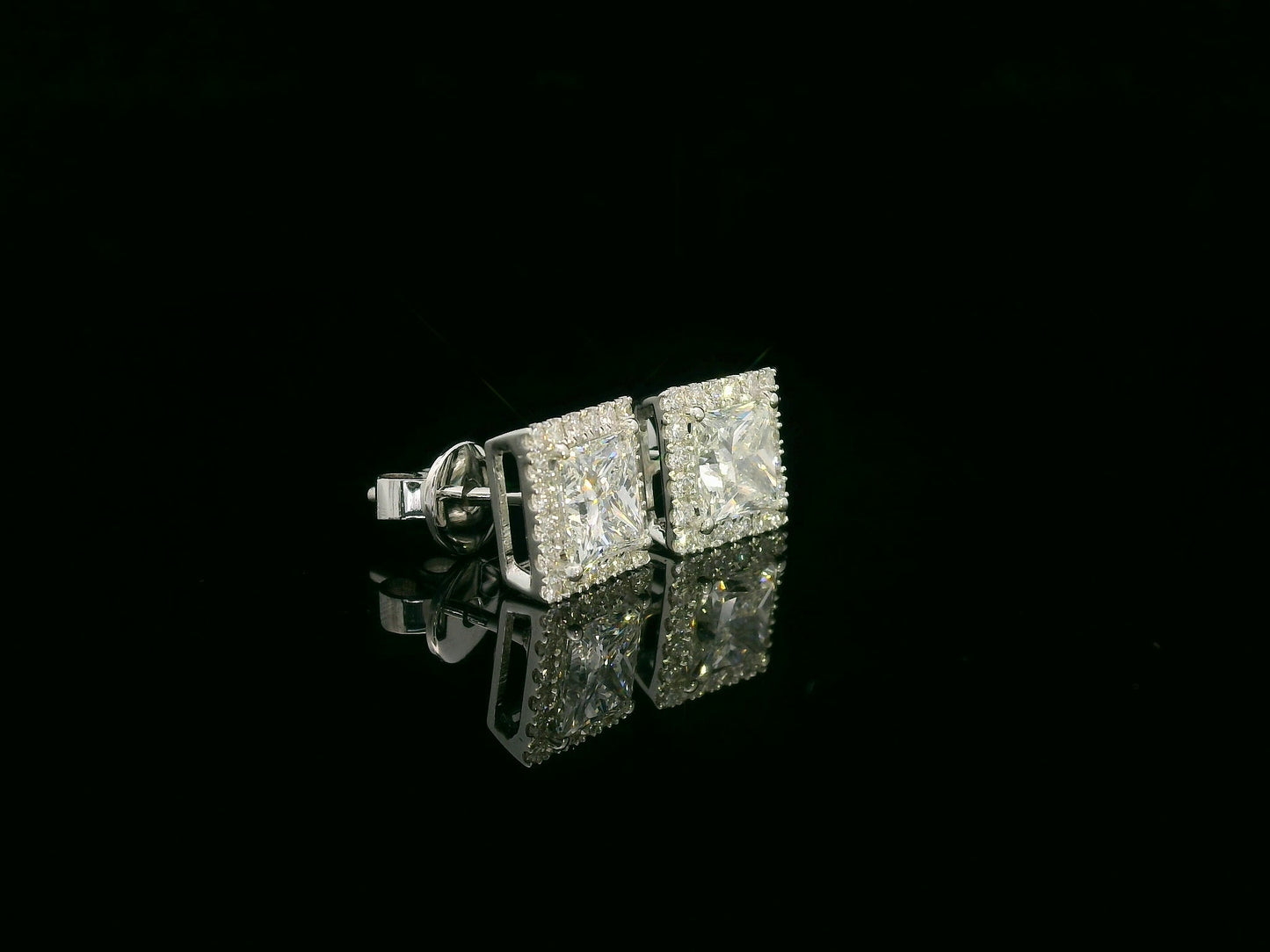 Princess cut diamond halo stud earrings in 18K white gold featuring GIA certified 1.01 carat E color VS2 diamonds with halo accents by Emirates Diamonds