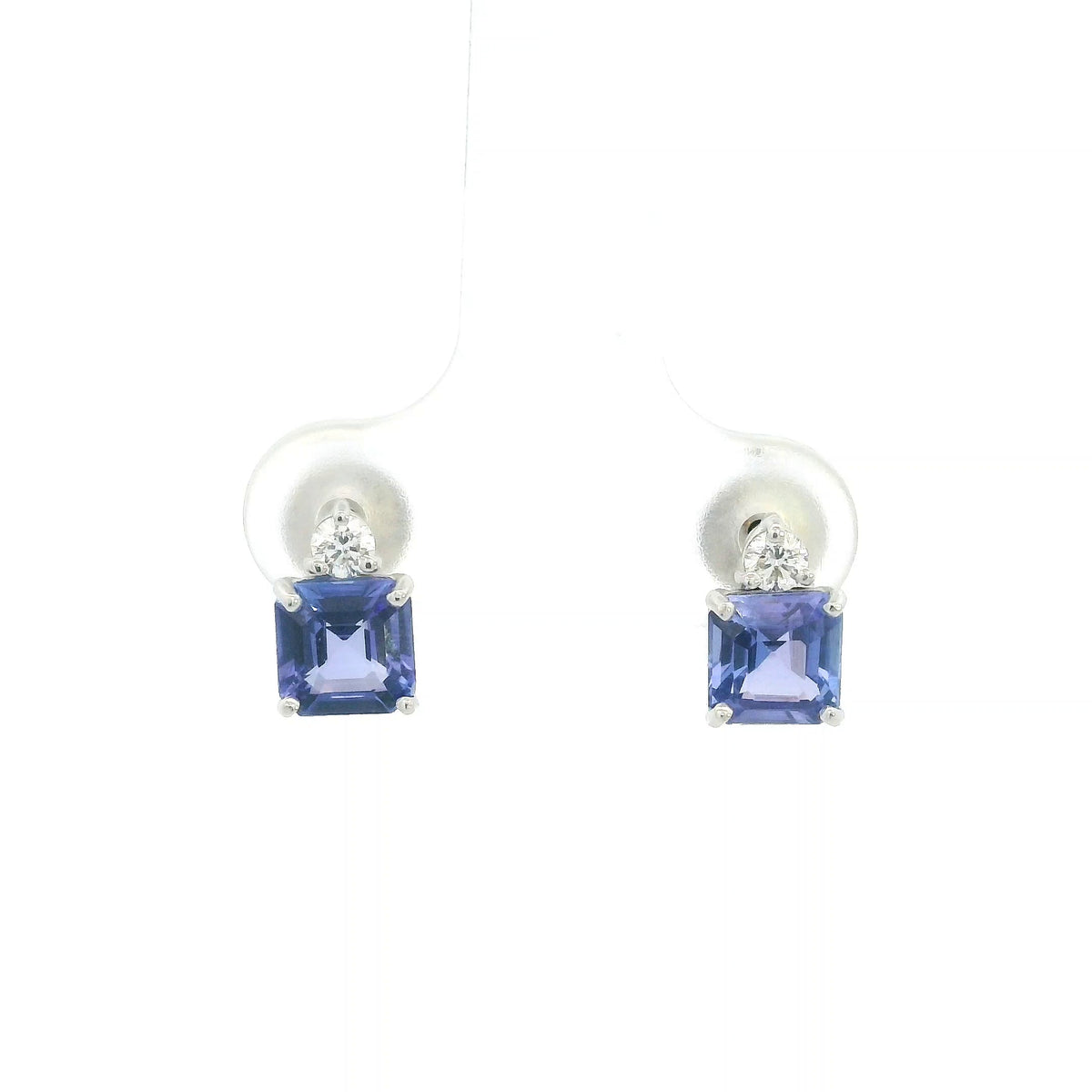 Pair of 18K white gold tanzanite and diamond stud earrings featuring square emerald-cut blue-violet tanzanites with a round diamond accent above each gemstone.