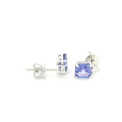 Pair of 18K white gold tanzanite and diamond stud earrings featuring square emerald-cut blue-violet tanzanites with a round diamond accent above each gemstone.