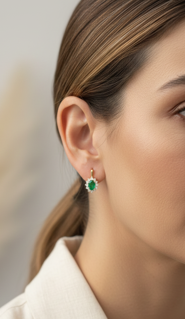 18K yellow gold emerald and diamond halo earrings featuring oval-cut emeralds surrounded by brilliant diamonds by Emirates Diamonds.