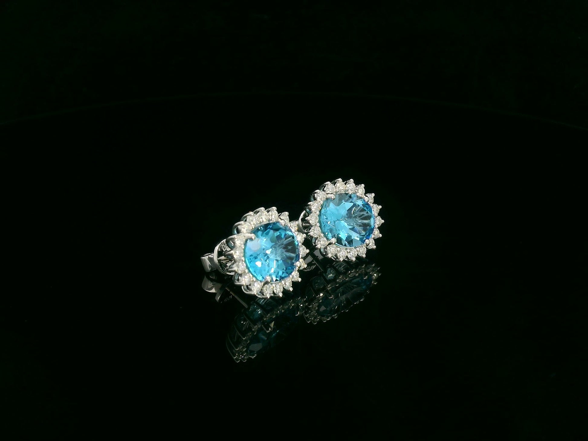18K white gold stud earrings featuring oval Swiss blue topaz gemstones surrounded by diamond halos
