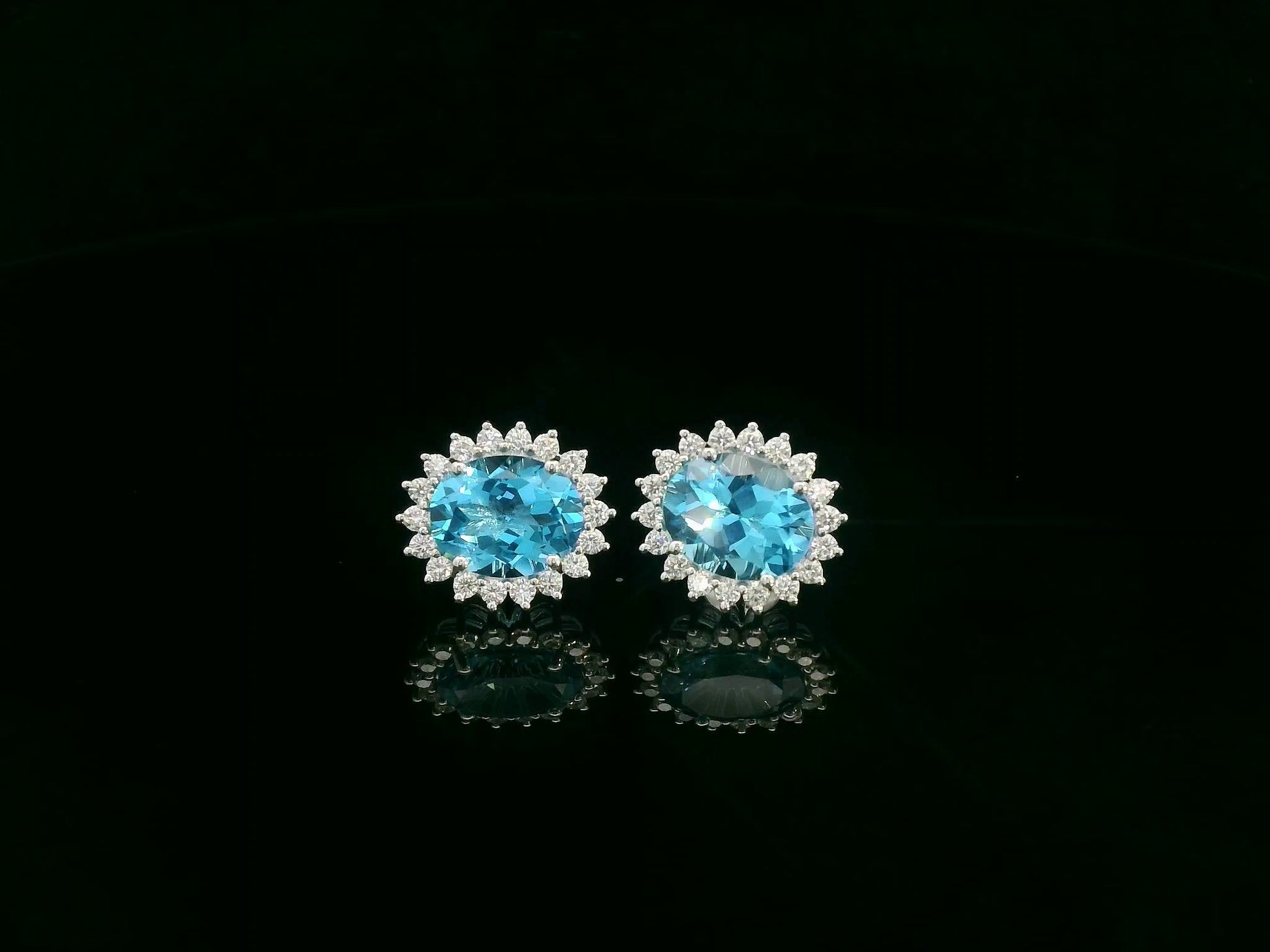 18K white gold stud earrings featuring oval Swiss blue topaz gemstones surrounded by diamond halos