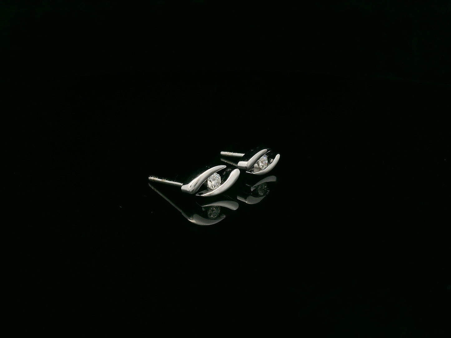 18K white gold modern diamond stud earrings with sculptural swirl design and round diamonds, total diamond weight 0.12 carat, Emirates Diamonds.