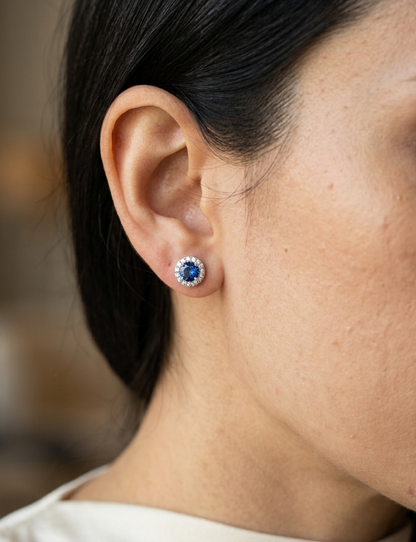 18K white gold sapphire halo stud earrings featuring 1.06 carats of blue sapphires surrounded by 0.16 carats of natural diamonds.