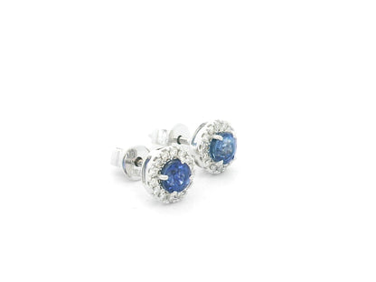 18K white gold sapphire halo stud earrings featuring 1.06 carats of blue sapphires surrounded by 0.16 carats of natural diamonds.