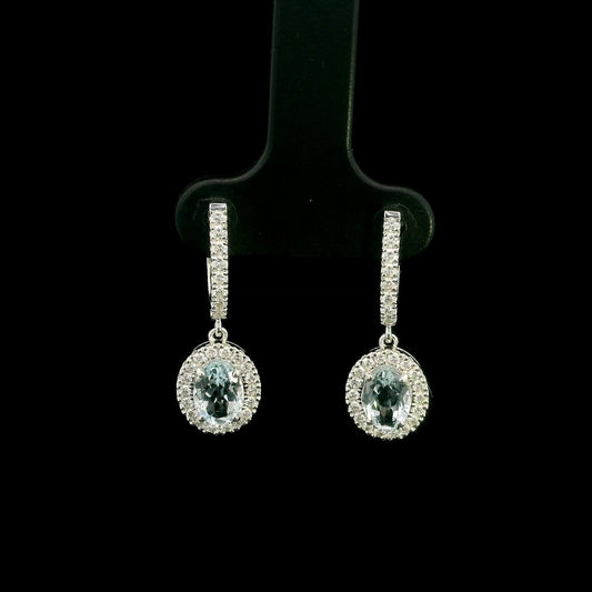 18K White Gold Aquamarine Drop Earrings featuring 1.50 carats of natural oval aquamarines surrounded by diamond halos with diamond huggie hoops and 0.48 carat natural diamonds.