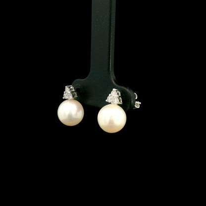 18K white gold freshwater pearl stud earrings featuring 7.5 × 8 mm freshwater pearls with a natural round diamond three-stone cluster and secure butterfly backs.