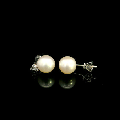 18K white gold freshwater pearl stud earrings featuring 7.5 × 8 mm freshwater pearls with a natural round diamond three-stone cluster and secure butterfly backs.