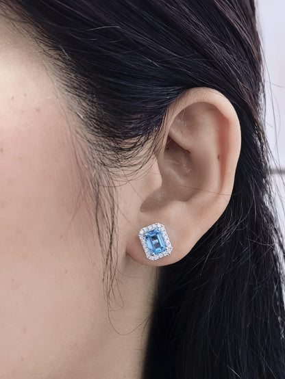 Blue Topaz diamond halo stud earrings in 18K white gold featuring 2.36 carats of natural emerald-cut Blue Topaz and 0.32 carat natural diamonds.