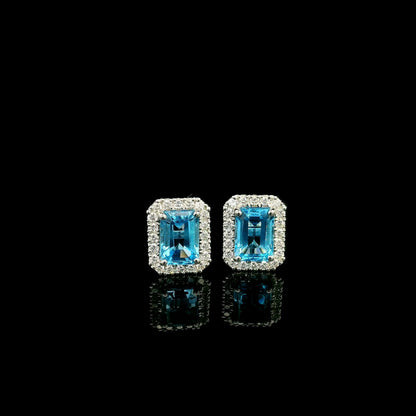 Blue Topaz diamond halo stud earrings in 18K white gold featuring 2.36 carats of natural emerald-cut Blue Topaz and 0.32 carat natural diamonds.