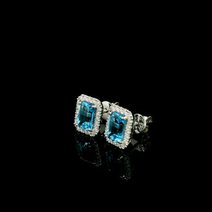 Blue Topaz diamond halo stud earrings in 18K white gold featuring 2.36 carats of natural emerald-cut Blue Topaz and 0.32 carat natural diamonds.