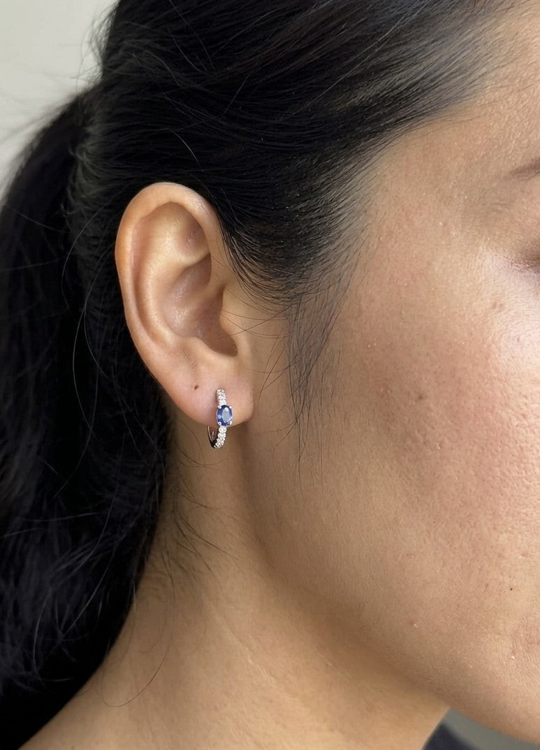 18K white gold blue sapphire and diamond huggie hoop earrings featuring oval blue sapphires and diamond-set hoops.
