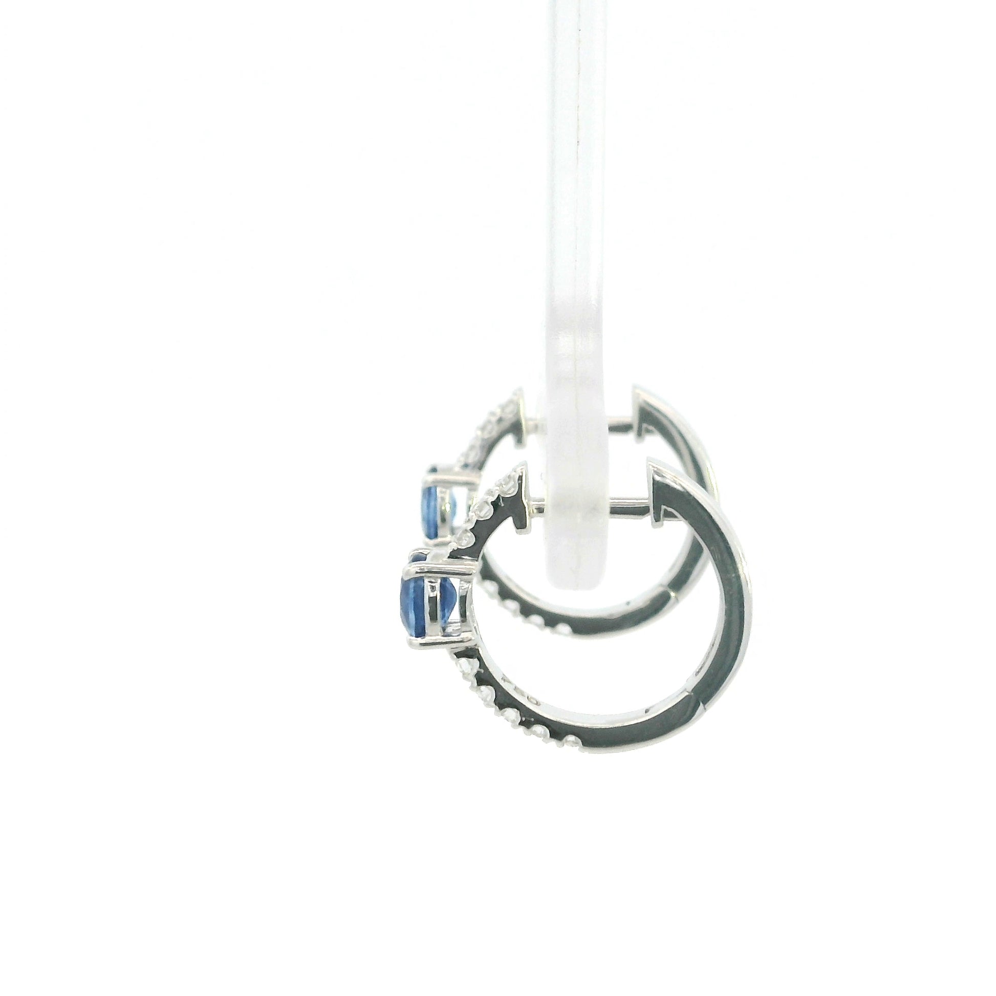 18K white gold blue sapphire and diamond huggie hoop earrings featuring oval blue sapphires and diamond-set hoops.