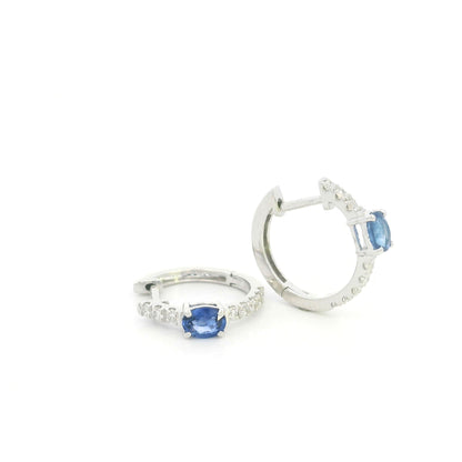 18K white gold blue sapphire and diamond huggie hoop earrings featuring oval blue sapphires and diamond-set hoops.