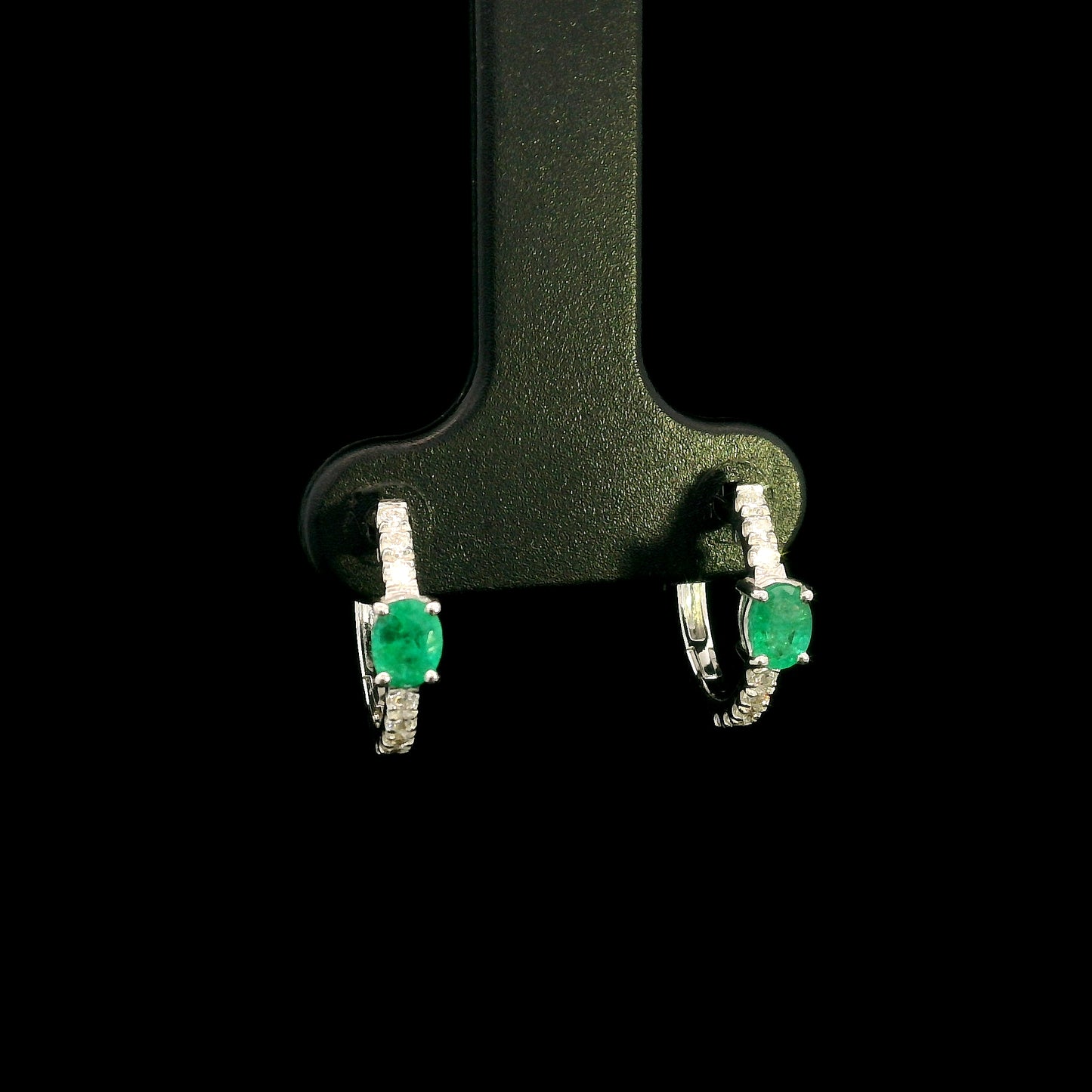 18K white gold emerald and diamond huggie hoop earrings featuring oval green emeralds and diamond-set hoops.