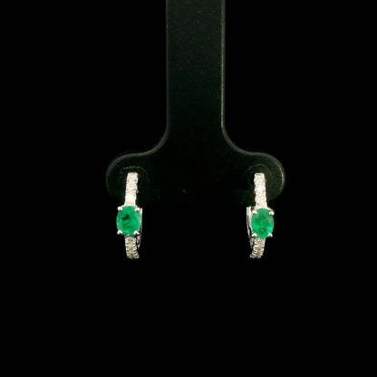 18K white gold emerald and diamond huggie hoop earrings featuring oval green emeralds and diamond-set hoops.
