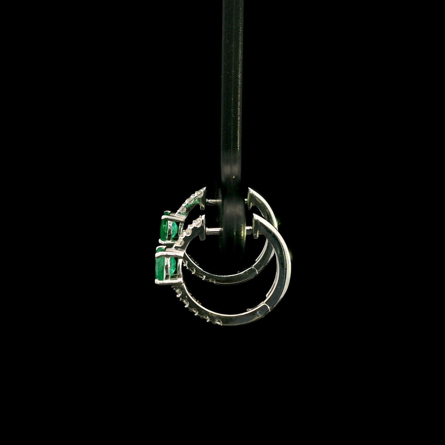 18K white gold emerald and diamond huggie hoop earrings featuring oval green emeralds and diamond-set hoops.