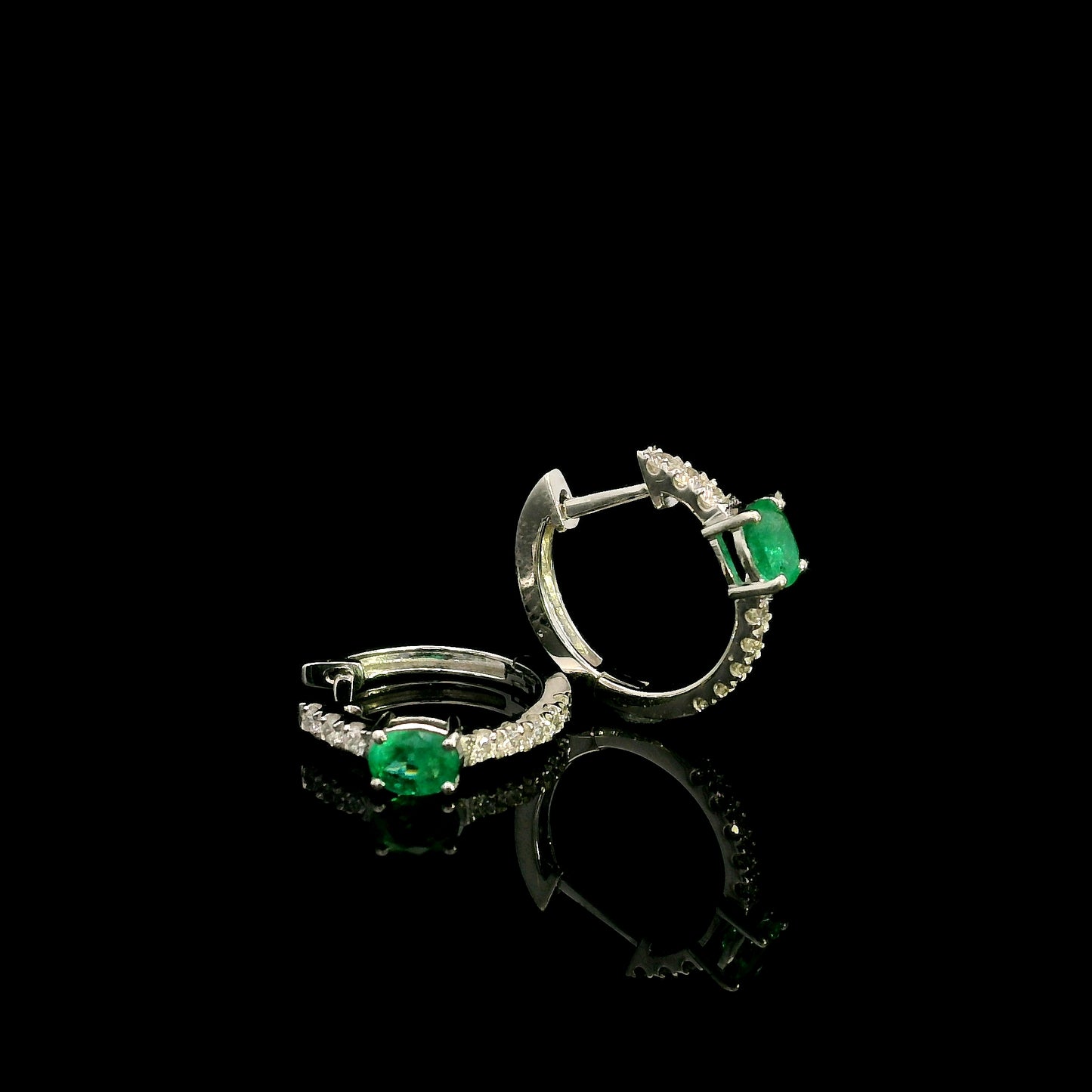 18K white gold emerald and diamond huggie hoop earrings featuring oval green emeralds and diamond-set hoops.