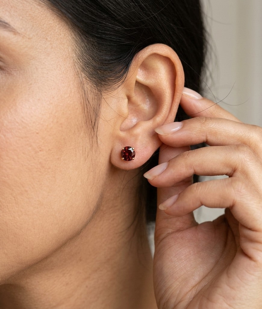 Round garnet solitaire stud earrings in 18K yellow gold with classic four-prong settings by Emirates Diamonds.