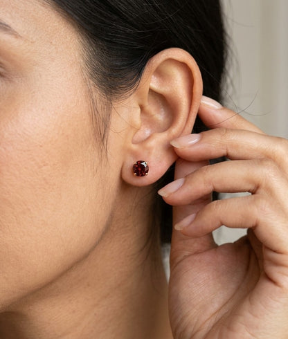 Round garnet solitaire stud earrings in 18K yellow gold with classic four-prong settings by Emirates Diamonds.
