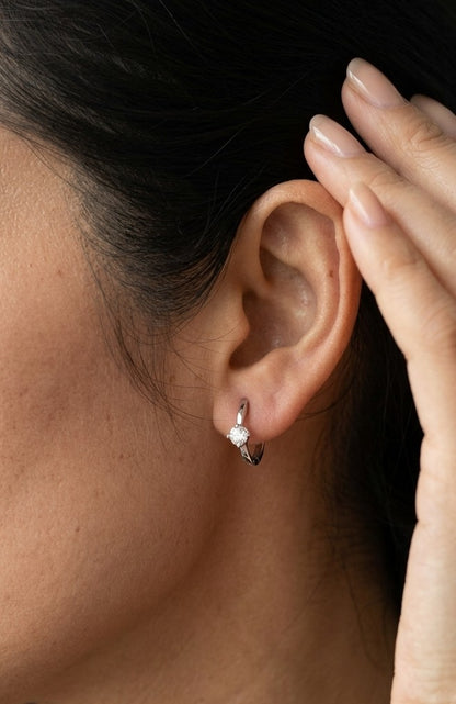 18K white gold huggie hoop earrings featuring a round diamond in a four-prong setting on each polished hoop.