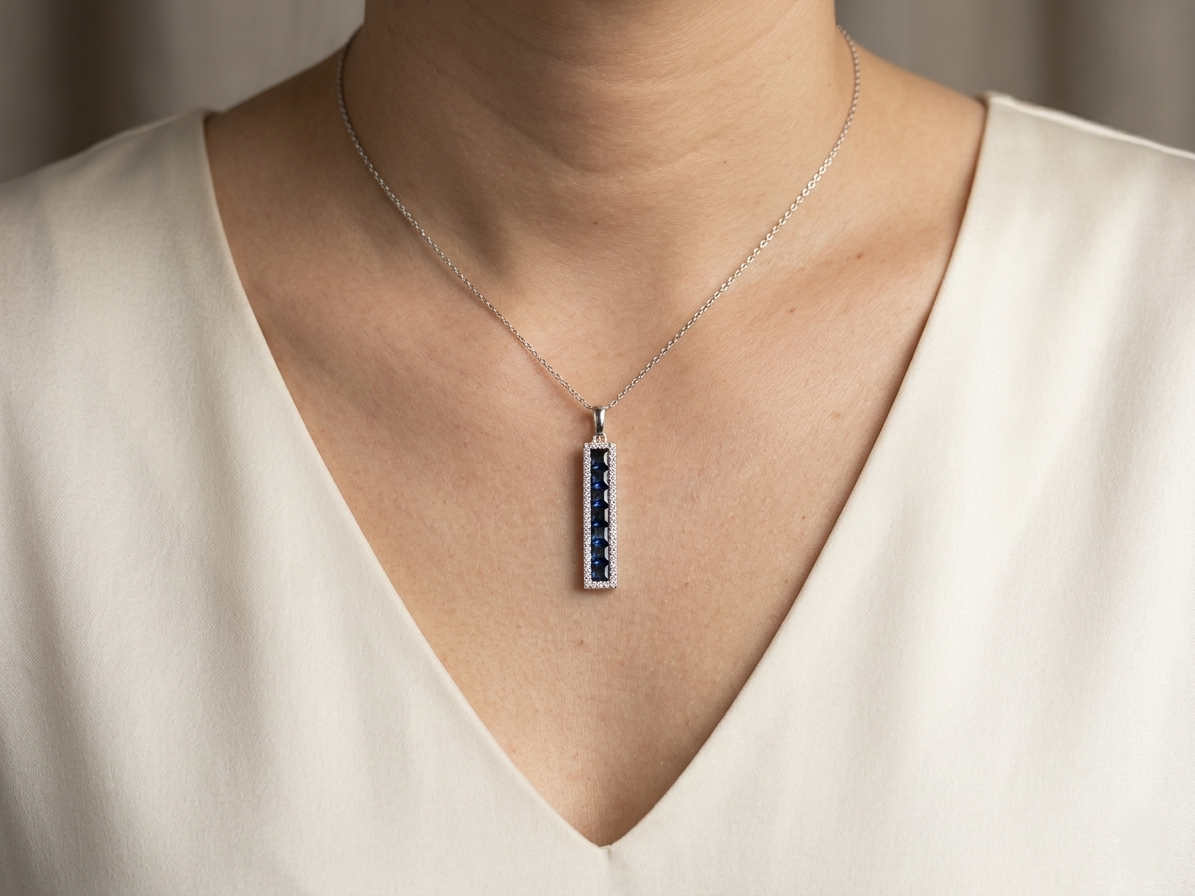 18K white gold sapphire bar pendant featuring 1.34 carats of princess cut blue sapphires surrounded by a diamond halo totaling 0.20 carat.