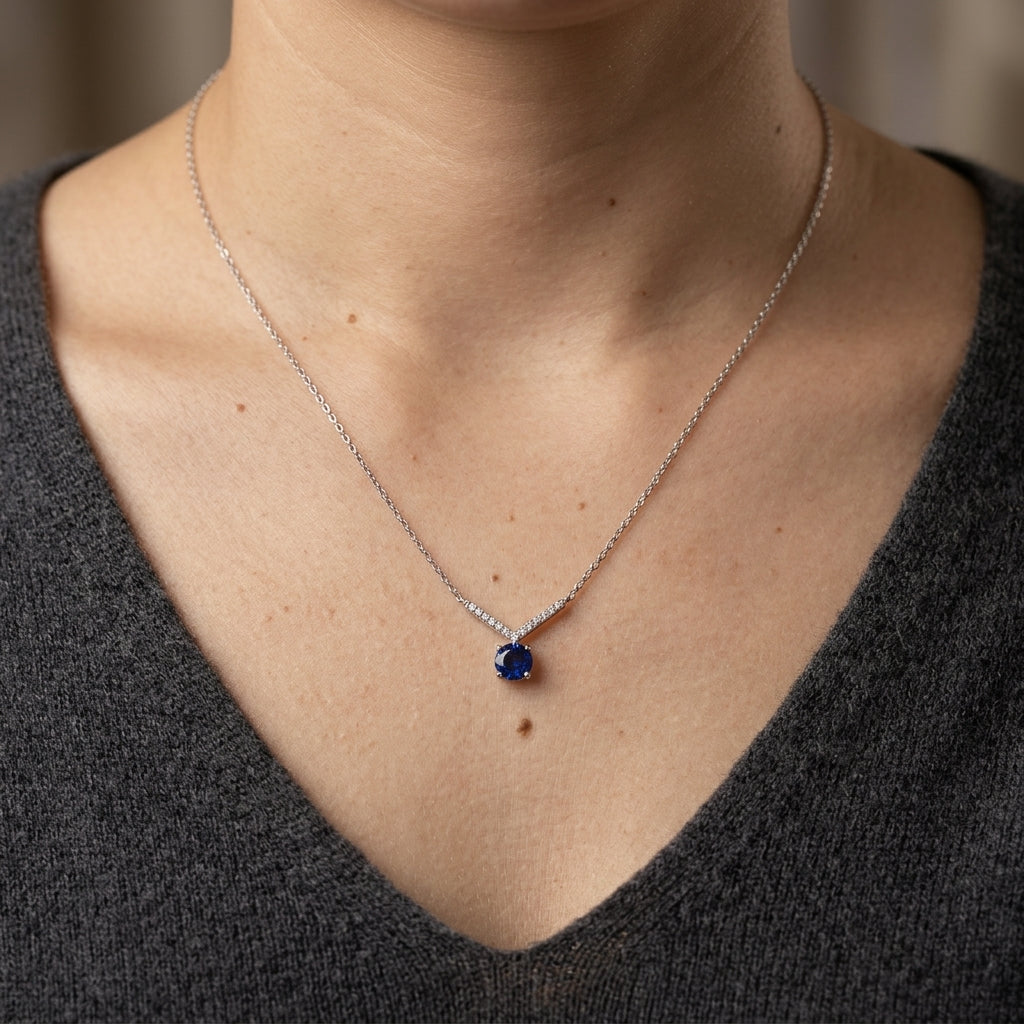Blue sapphire and diamond necklace in 18K white gold featuring a 0.95 carat round blue sapphire in a four-prong setting beneath a V-shaped diamond-set design.
