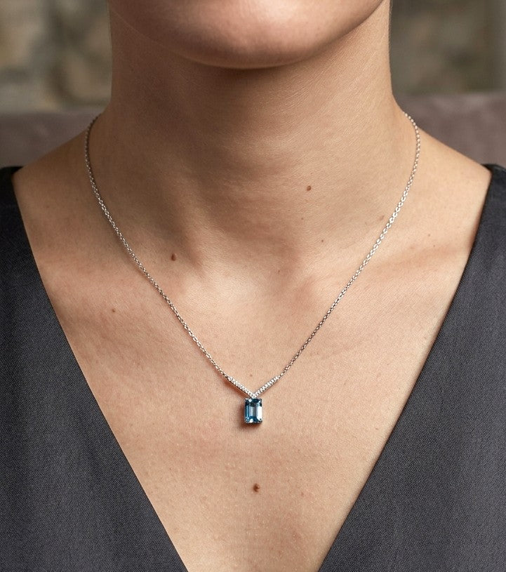 Blue topaz and diamond necklace in 18K white gold featuring a rectangular emerald-cut blue topaz suspended beneath a V-shaped arrangement of round diamonds.