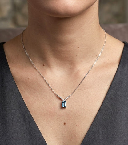 Blue topaz and diamond necklace in 18K white gold featuring a rectangular emerald-cut blue topaz suspended beneath a V-shaped arrangement of round diamonds.