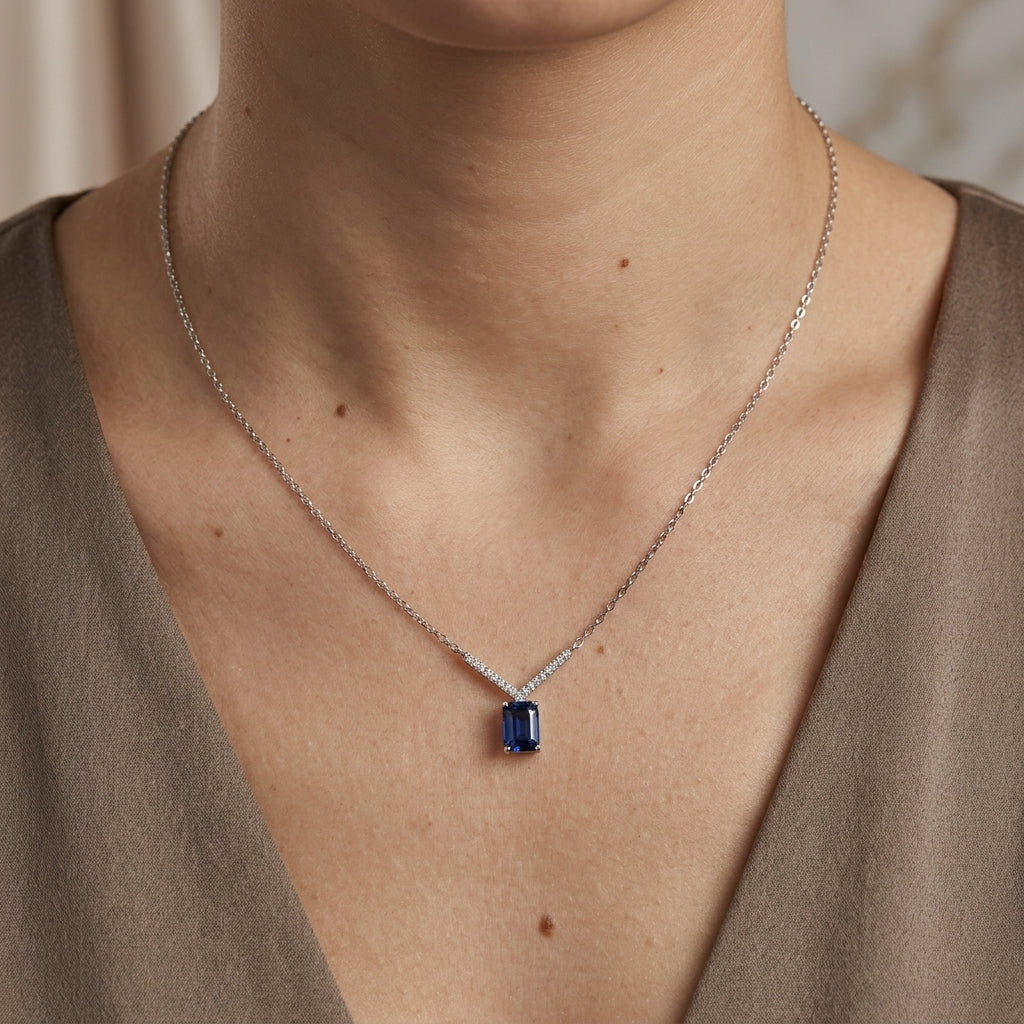 Blue sapphire and diamond necklace in 18K white gold featuring a rectangular emerald-cut sapphire suspended beneath a V-shaped row of round diamonds.