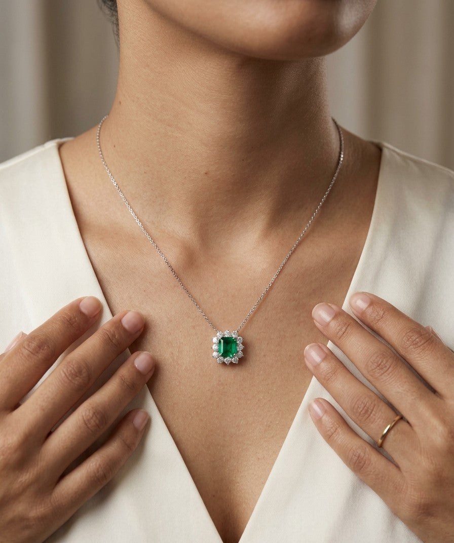 Emerald and diamond cluster halo necklace in 18K white gold featuring a 2.53 carat rectangular emerald surrounded by round diamonds totalling 1.46 carats, suspended from a fine white gold chain.