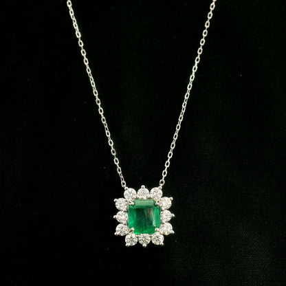 Emerald and diamond cluster halo necklace in 18K white gold featuring a 2.53 carat rectangular emerald surrounded by round diamonds totalling 1.46 carats, suspended from a fine white gold chain.