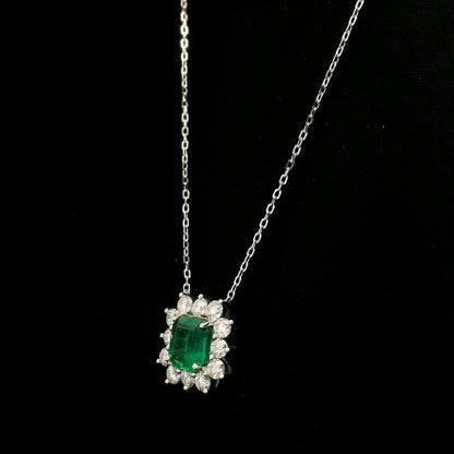 Emerald and diamond cluster halo necklace in 18K white gold featuring a 2.53 carat rectangular emerald surrounded by round diamonds totalling 1.46 carats, suspended from a fine white gold chain.