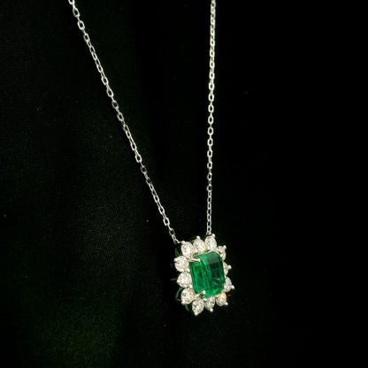 Emerald and diamond cluster halo necklace in 18K white gold featuring a 2.53 carat rectangular emerald surrounded by round diamonds totalling 1.46 carats, suspended from a fine white gold chain.