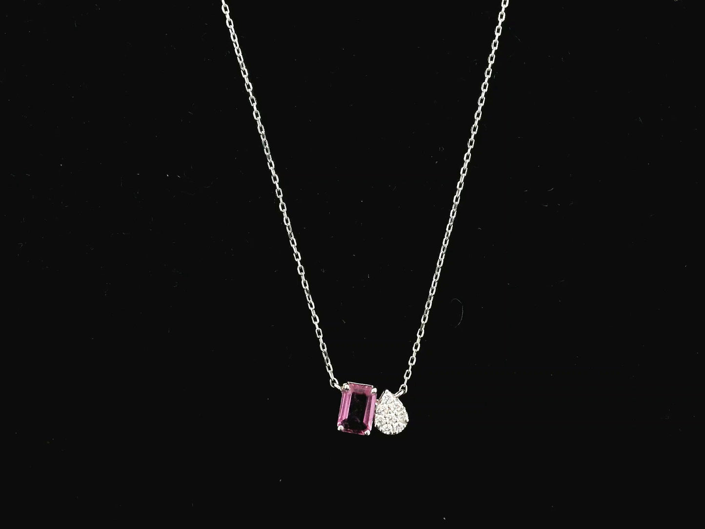 18K white gold pendant necklace featuring a 0.63 carat emerald cut pink sapphire paired with a 0.07 carat pear shaped diamond.