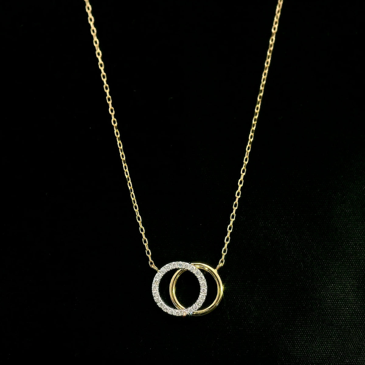 Interlocking diamond circle necklace in 18K yellow gold with one diamond-set circle and one polished gold circle.