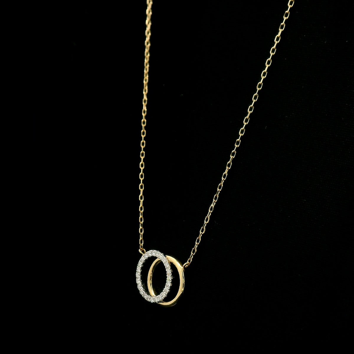 Interlocking diamond circle necklace in 18K yellow gold with one diamond-set circle and one polished gold circle.