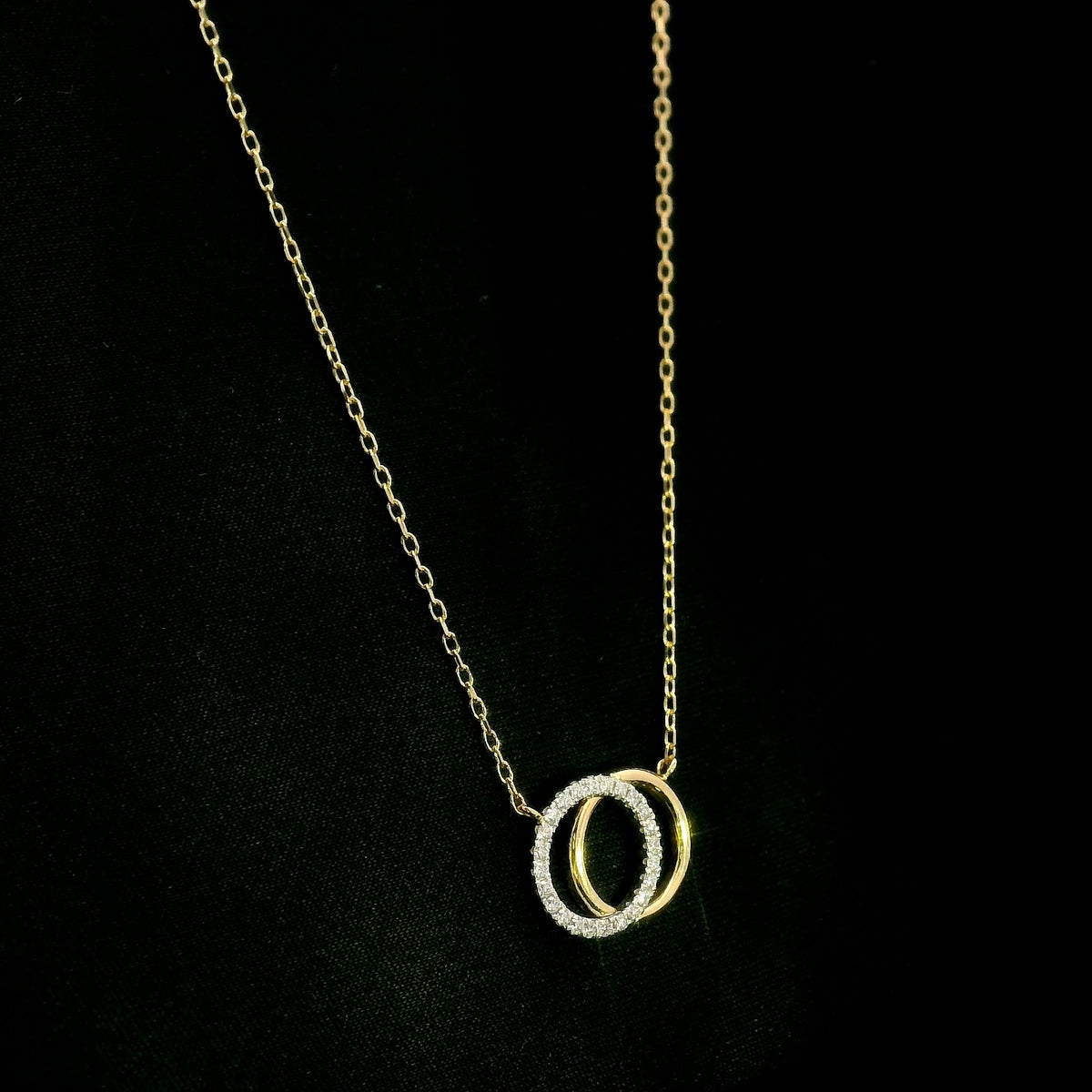 Interlocking diamond circle necklace in 18K yellow gold with one diamond-set circle and one polished gold circle.