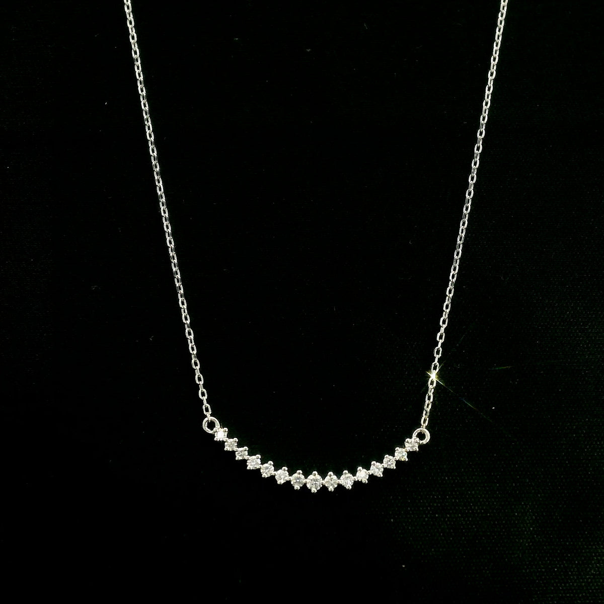 Diamond curved bar necklace in 18K white gold featuring a gently curved row of round diamonds with a total weight of 0.18 carat, connected to a fine white gold chain.