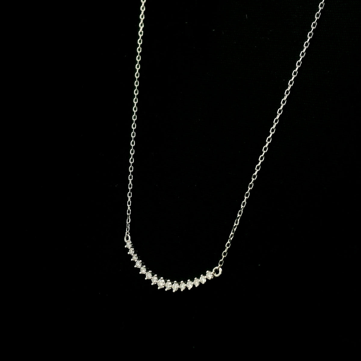 Diamond curved bar necklace in 18K white gold featuring a gently curved row of round diamonds with a total weight of 0.18 carat, connected to a fine white gold chain.