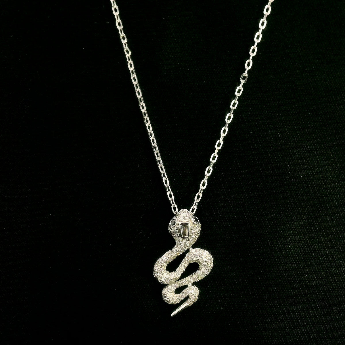 18K white gold snake pendant necklace featuring a curved serpent with round diamonds along its coiled body, a detailed head and a polished tapered tail.