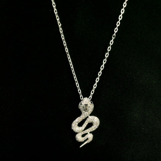 18K white gold snake pendant necklace featuring a curved serpent with round diamonds along its coiled body, a detailed head and a polished tapered tail.