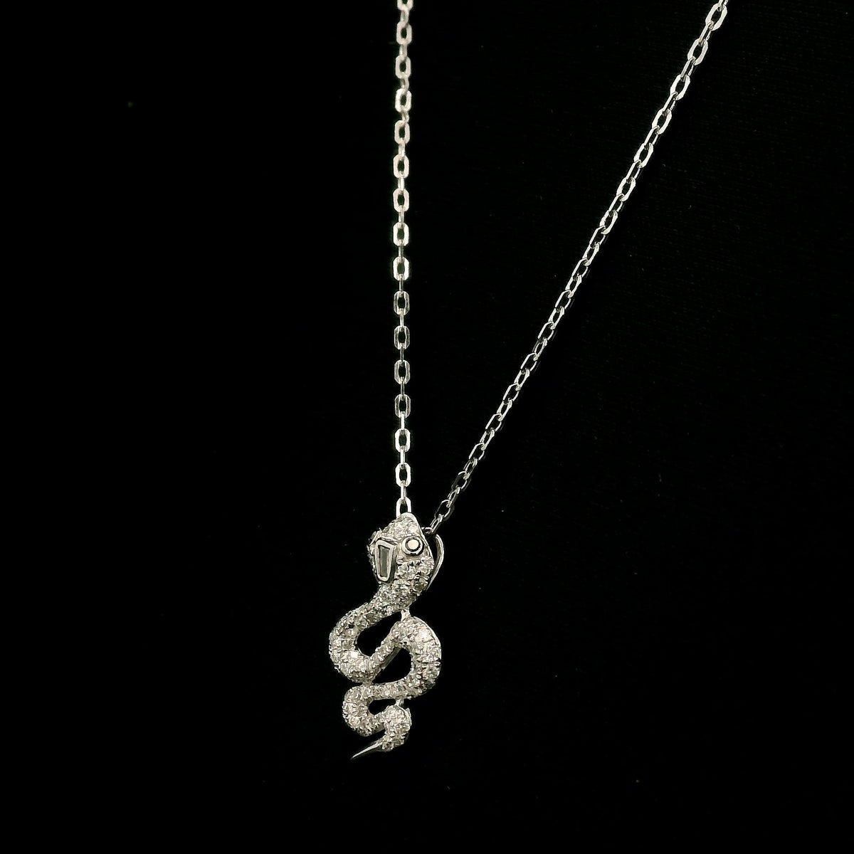 18K white gold snake pendant necklace featuring a curved serpent with round diamonds along its coiled body, a detailed head and a polished tapered tail.