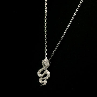18K white gold snake pendant necklace featuring a curved serpent with round diamonds along its coiled body, a detailed head and a polished tapered tail.