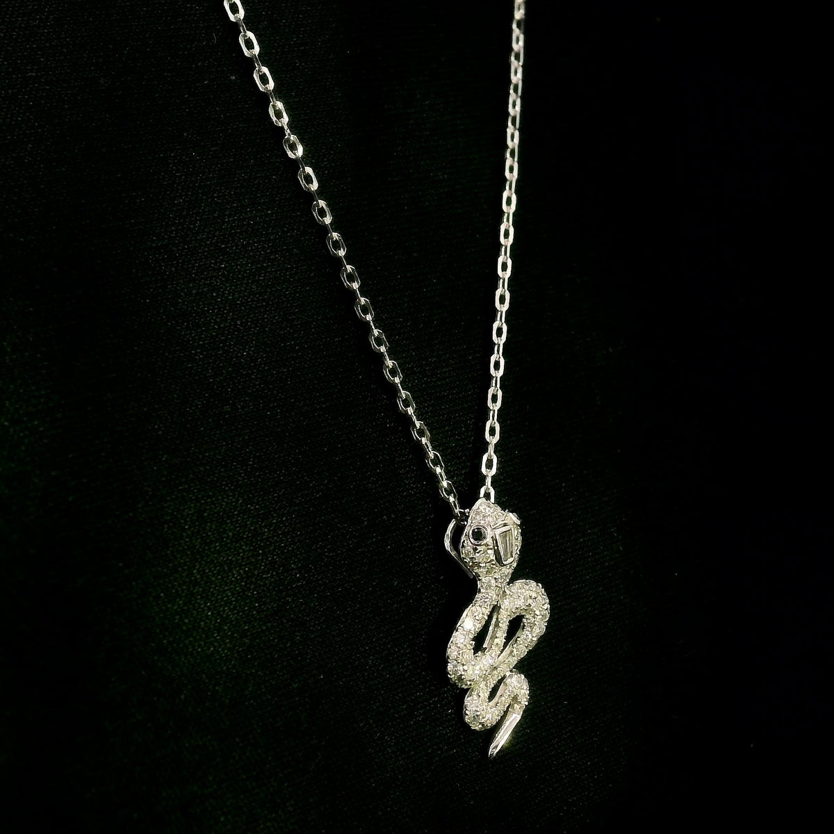 18K white gold snake pendant necklace featuring a curved serpent with round diamonds along its coiled body, a detailed head and a polished tapered tail.