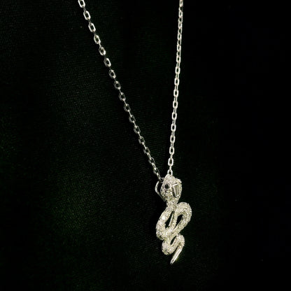 18K white gold snake pendant necklace featuring a curved serpent with round diamonds along its coiled body, a detailed head and a polished tapered tail.
