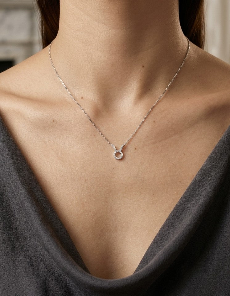 Taurus zodiac necklace in 18K white gold with natural diamonds set along the Taurus symbol, suspended from a chain.