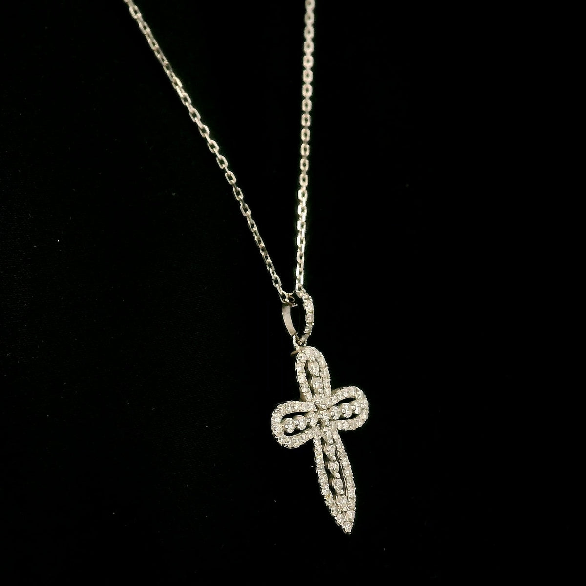 Openwork diamond cross pendant in 18K white gold with round diamond borders, central diamond accents and a diamond-set bail, displayed on a chain.